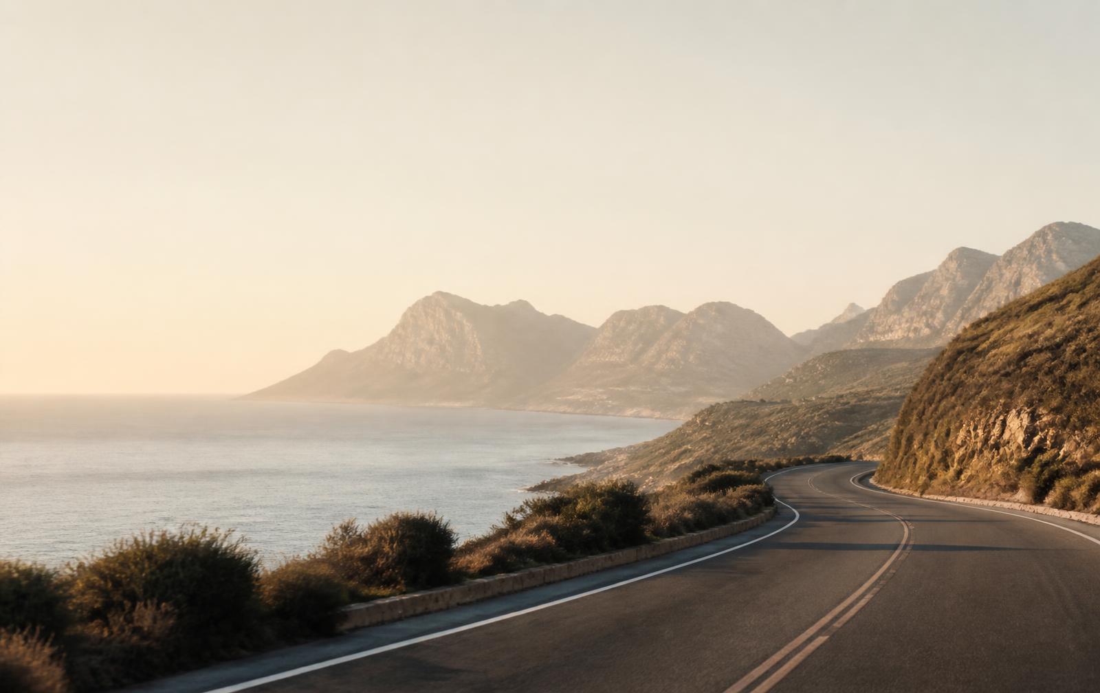 An empty coastal road curving toward distant mountains at golden hour